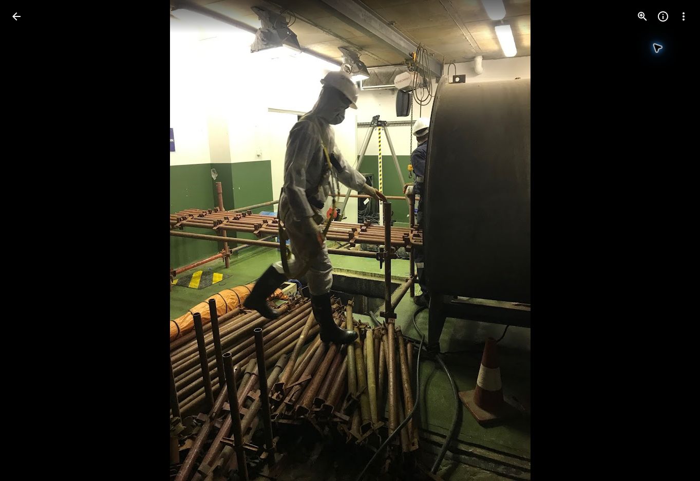 Worker in protective equipment on scaffolding inside a contaminated tank work area